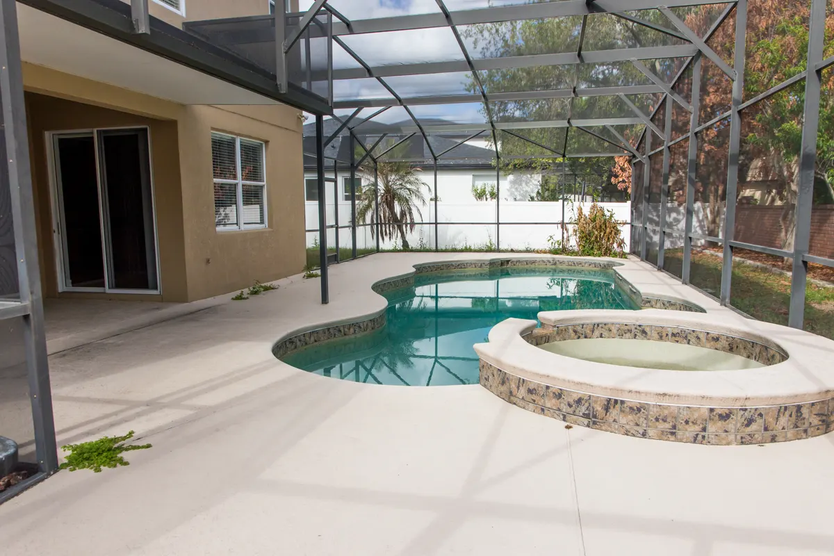 Current condition: screened pool with raised circular spa, pool deck, and the rear facade of the residence.