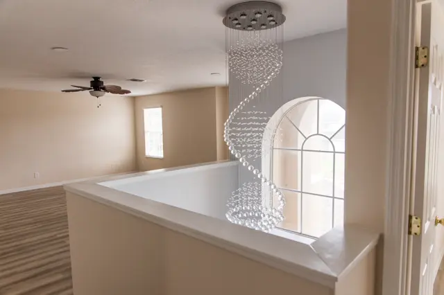 Current condition staircase overlook with spiral crystal chandelier and arched window.